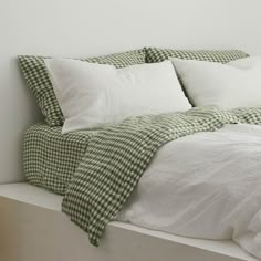 a bed with white sheets and green gingham checkered pillow cases on it