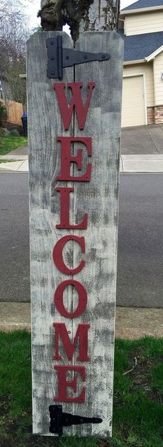 a wooden sign that says welcome on the side of a road in front of a house