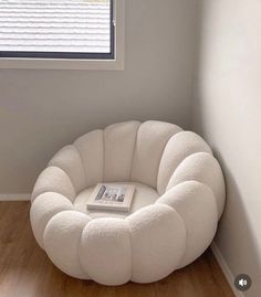 a white chair sitting in front of a window next to a book on top of a wooden floor