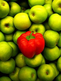 a red pepper sitting on top of green apples in the shape of a heart shaped tomato