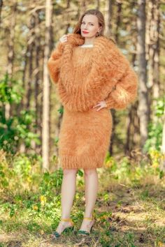 a woman is standing in the woods wearing a fuzzy orange coat and heels with her hands on her hips