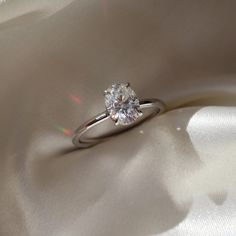 a diamond ring sitting on top of a white satin material covered in light glares