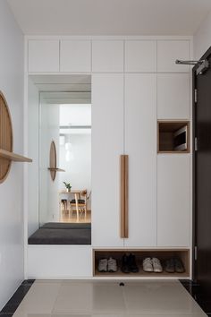 a room with white walls and black flooring next to a wooden shelf filled with shoes