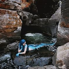 a woman with blue hair is laying on rocks in the water