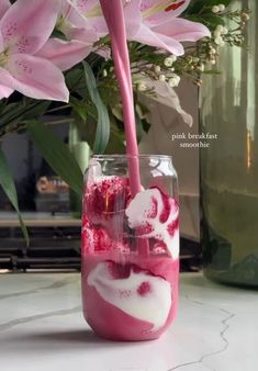 a vase with pink flowers in it sitting on a table next to a glass filled with liquid