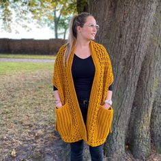 a woman standing next to a tree wearing a yellow knitted cardigan