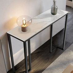 a white marble table with a black metal base and a glass vase on top, next to a wall