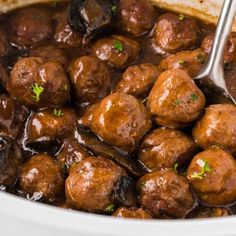 meatballs and mushrooms are being cooked in a slow cooker with a ladle