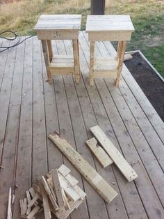 two small wooden tables sitting on top of a wooden deck next to a pile of wood