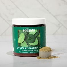 a jar of soilia powder next to a spoon on a marble countertop with green leaves in the background