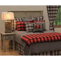 a bed with red and black plaid pillows on it's headboard next to a night stand