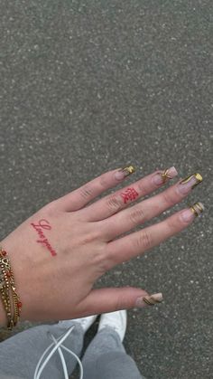 a woman's hand with gold and red nail polish on it, while she is holding out her left hand