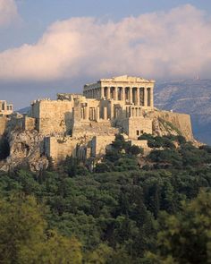 an old building on top of a hill with trees in the foreground and mountains in the background