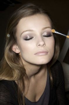 a woman with makeup brushes in her eyes and eye shadow on her face, looking at the camera