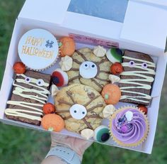 a person holding up a box filled with halloween cookies and cupcakes on top of it