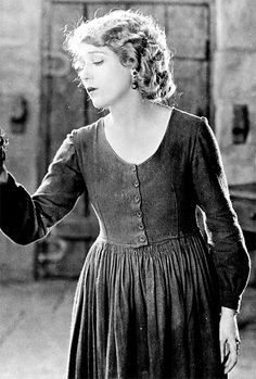 an old black and white photo of a woman holding something in her hand while wearing a dress