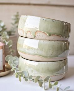 three green ceramic bowls sitting on top of a table next to a candle and some plants