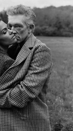 a man and woman kissing each other in the middle of a field with trees behind them