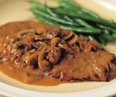 a white plate topped with meat covered in mushroom gravy next to green beans