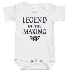 Rapunzie's adorable baby onesie, perfect for little ones who are destined to become legends! Made from 100% cotton, this short-sleeve onesie ensures utmost comfort for your precious bundle of joy. With its charming design featuring the iconic Legend of Zelda video game symbol and the captivating caption, "Legend in the Making," your baby will surely make a statement wherever they go.Crafted with love and attention to detail, this baby onesie combines style and softness to create a delightful out Father's Day Gift Cotton Onesie, Funny Customizable Short Sleeve Onesie, Funny Short Sleeve Onesie As A Gift, Funny Short Sleeve Onesie As Gift, Cotton Onesie For Father's Day, Pre-shrunk Short Sleeve Onesie For Playtime, White Short Sleeve Onesie With Character Print, Customizable Cotton Onesie For Father's Day, Short Sleeve Onesie For Father's Day Gift