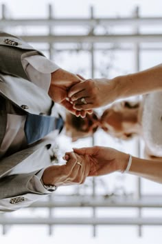 the bride and groom hold hands as they stand next to each other in front of a window