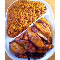 a white plate topped with meat and beans next to a bowl filled with baked beans