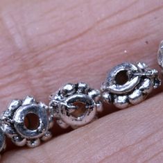 a close up of a person's hand with some silver beads on the bracelet