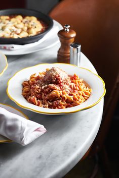 two plates of pasta with meat and sauce on the table next to a casserole dish