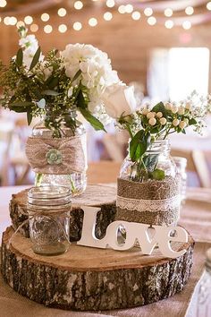 two mason jars filled with flowers are sitting on top of a wooden slice that says love