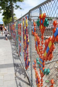 a fence that has some kind of colorful thing on it, along with people walking down the sidewalk