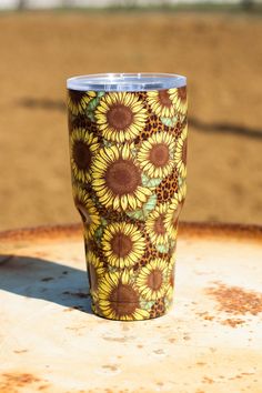 a yellow and brown sunflower pattern tumbler cup sitting on top of a rusted metal table