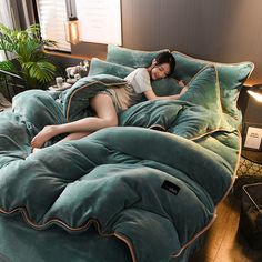 a woman laying on top of a green comforter in a bed with lots of pillows