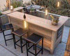 an outdoor bar with three stools next to it and lights hanging from the ceiling