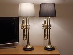 two brass trumpet lamps sitting on top of a wooden table next to a flat screen tv