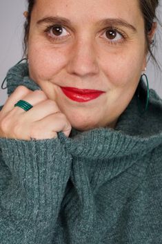 a woman with her hand on her shoulder and wearing a green turtle neck sweater, smiling at the camera