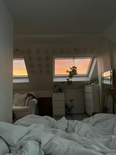 an unmade bed with white sheets and pillows in a loft space under two windows