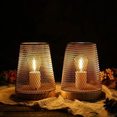 two lit candles sitting next to each other on top of a cloth covered tablecloth