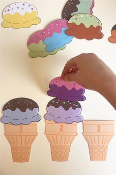 a hand is reaching for an ice cream cone cutout on the wall next to several cupcakes