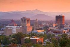 a city with mountains in the background and buildings at sunset or sunrise, as seen from an overlook point