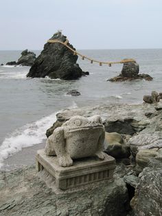 a stone statue sitting on top of a rocky beach next to the ocean with a rope hanging over it