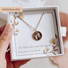 a person is holding a necklace with a baby's footprints on it in a box