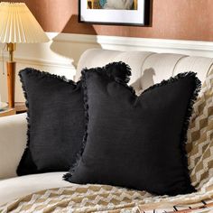 two black pillows sitting on top of a white couch next to a table with a lamp