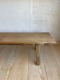 a wooden bench sitting on top of a hard wood floor next to a brick wall