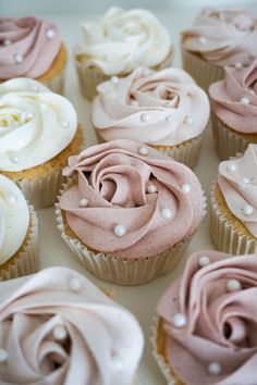 cupcakes with pink frosting and white icing are arranged in a box