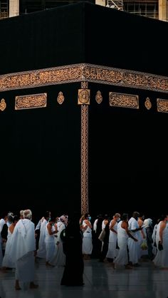 a group of people standing in front of a large black structure with gold writing on it