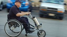 an older man in a wheel chair on the street with cars passing by behind him