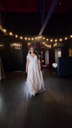 a woman in a white dress walking across a dark room with lights on the ceiling