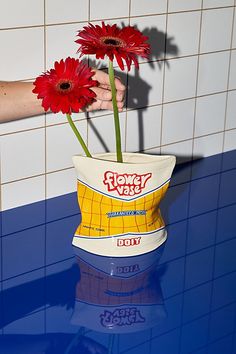 two red flowers in a paper bag on a blue counter with tile wall behind it