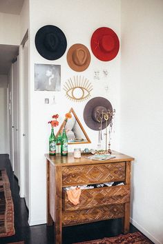 a dresser with hats on the wall above it and a rug in front of it