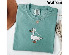 This is a Comfort Colors garment-dyed embroidered t-shirt; a spring tee made 100% with ring-spun cotton. The soft-washed, garment-dyed fabric brings extra coziness to your wardrobe while the relaxed fit makes it an excellent daily choice. The double-needle stitching throughout the embroidered goose tee makes it highly durable while the lack of side-seams helps this cute gift for her shirt retain its tubular shape. ** HOW TO ORDER 1. Check our photos for sizing and color options. 2. Select your size and color from the drop-down menus. 3. Click "ADD TO CART" to add the shirt to your cart. 4. Click "PROCEED TO CHECKOUT" to purchase your shirt. ** PRODUCTION TIME: 1-3 days (Usually 2 days) ** SHIPPING TIME: 2-5 days (Usually 3 days) ** DETAILS: This is a Comfort Colors garment-dyed embroidered Casual Embroidered Graphics T-shirt For Spring, Spring Green T-shirt With Embroidered Graphics, University Funny, Silly Goose University, Spring Tee, Spring Tees, Cute Gifts For Her, Silly Goose, Embroidered Tshirt